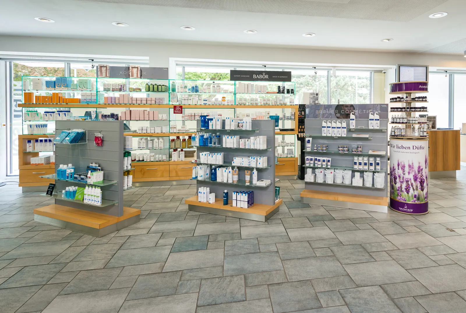 Regale mit Pflege- und Kosmetikprodukten in der Reichenauer Apotheke vor großen Fenstern