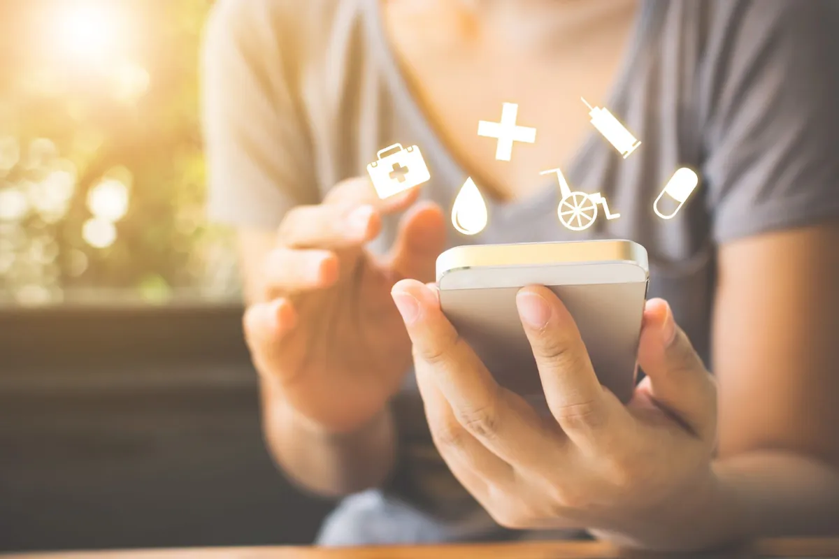 Hand mit Smartphone, darüber Symbole für Medikamente und Gesundheit
